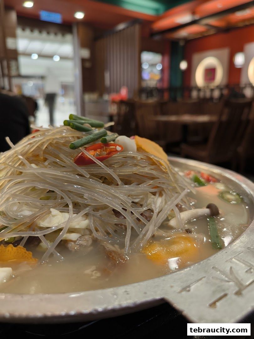 A close-up of a Korean BBQ hot pot dish with noodles, vegetables, and broth.