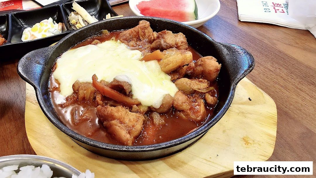 A sizzling Korean BBQ dish with chicken and melted cheese in a cast iron pan.