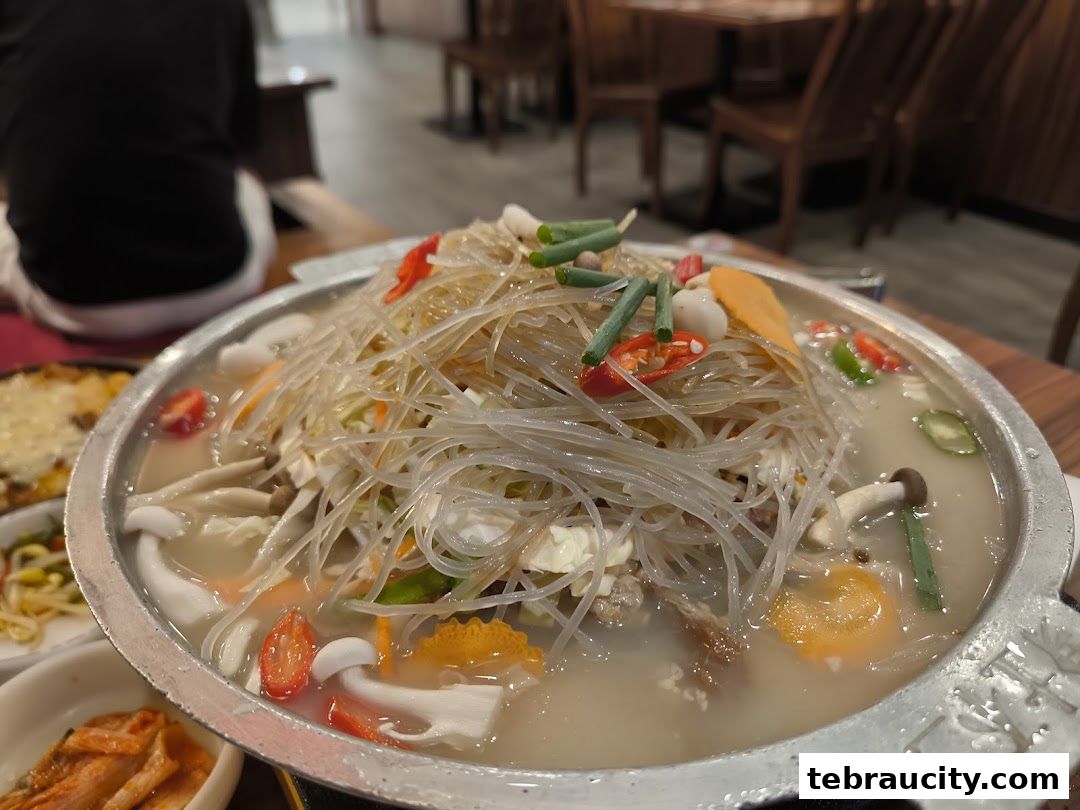 A close-up of a Korean hot pot dish with noodles, vegetables, and mushrooms.
