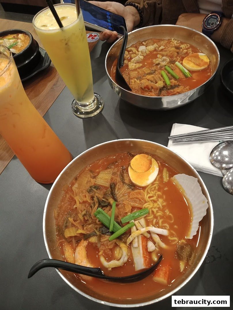 Two steaming bowls of Korean ramen with seafood and kimchi, alongside refreshing drinks.