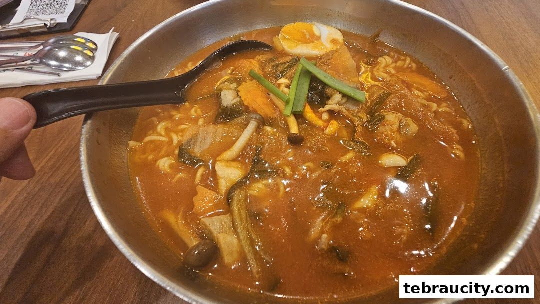 A close-up shot of a steaming bowl of Korean kimchi ramen with egg and vegetables.