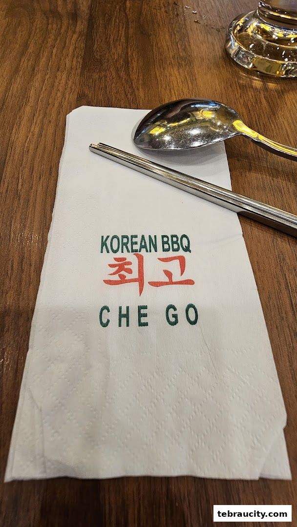 A napkin with Korean BBQ branding and chopsticks and spoon on a wooden table.