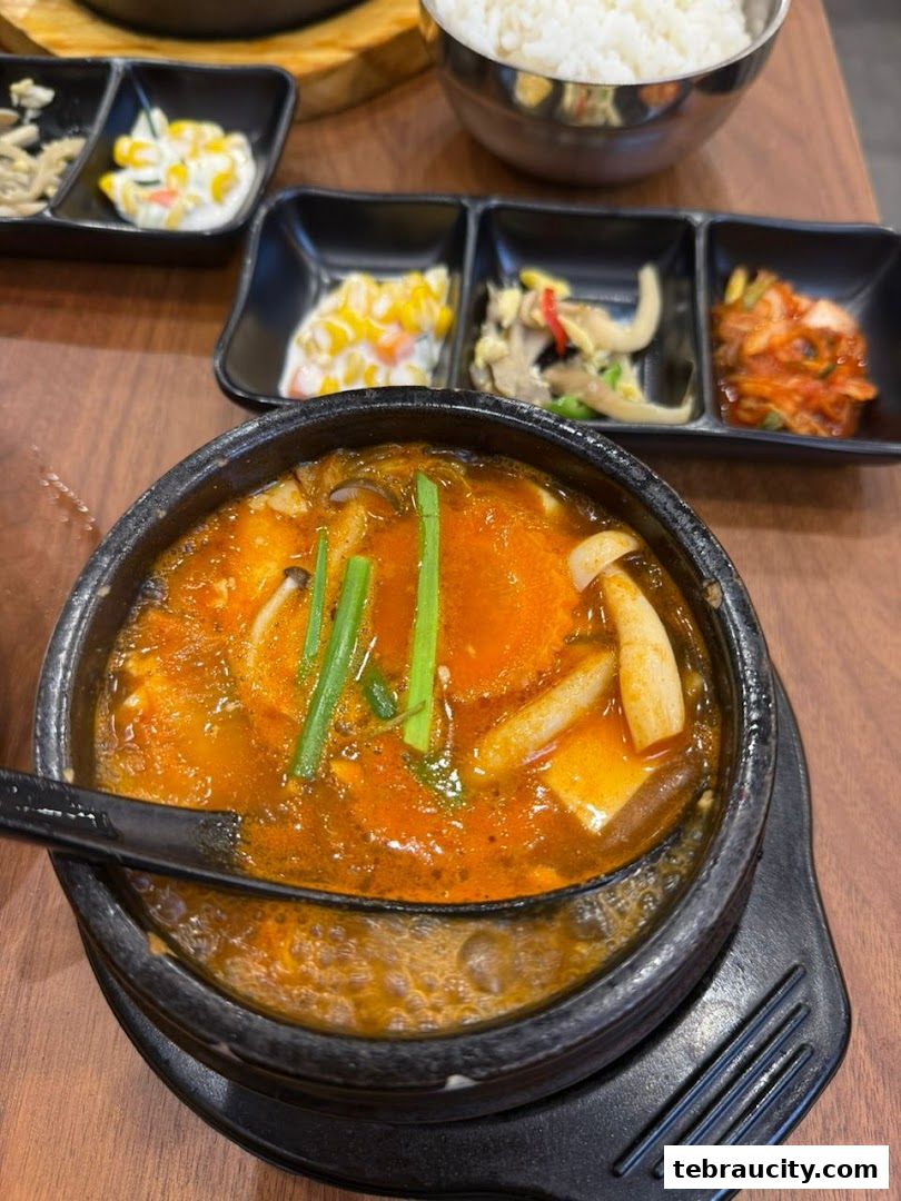 A steaming bowl of Korean tofu stew with side dishes and rice.
