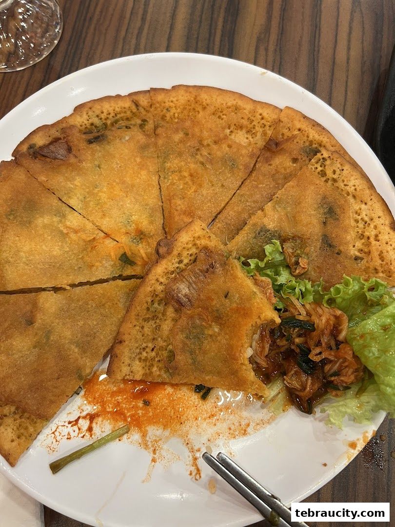 A delicious Korean pancake with kimchi and lettuce on a white plate.