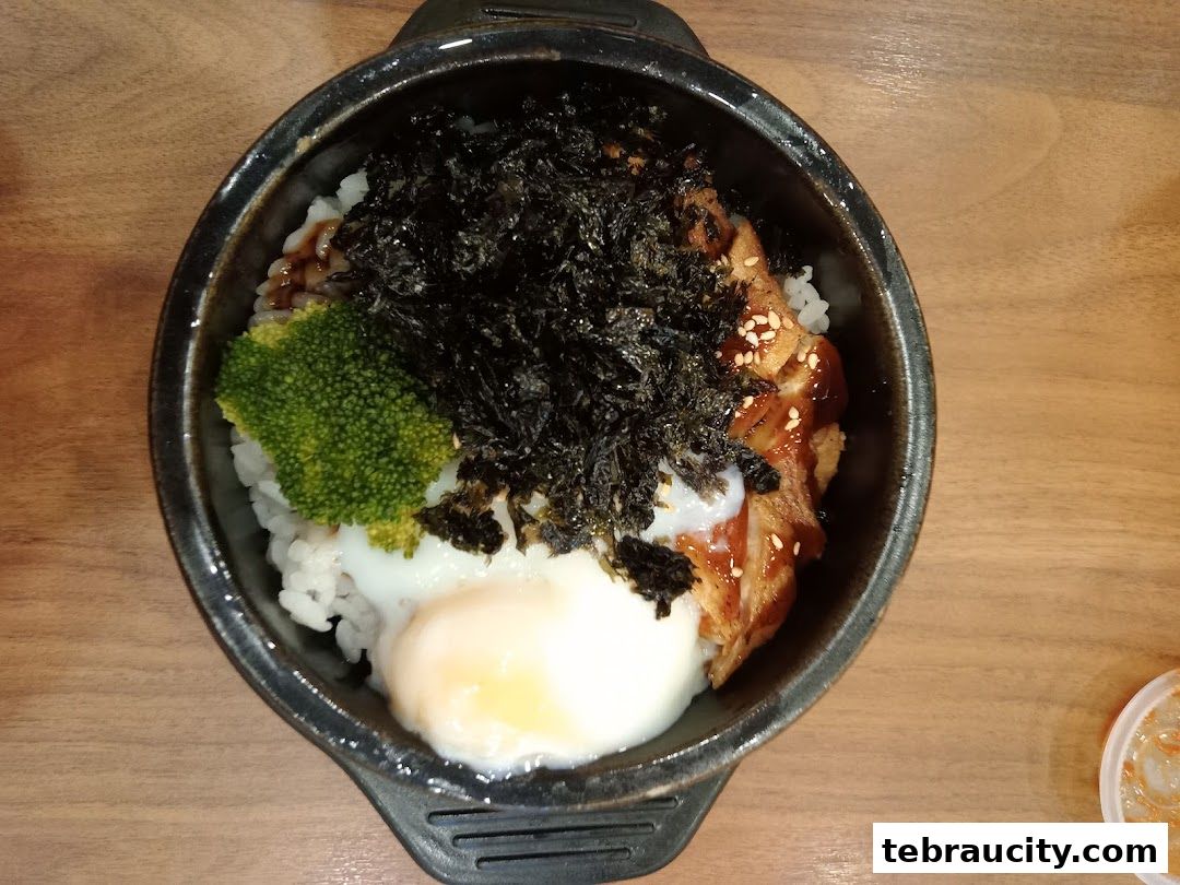 A top-down view of a Korean rice bowl with chicken, egg, broccoli, and seaweed.