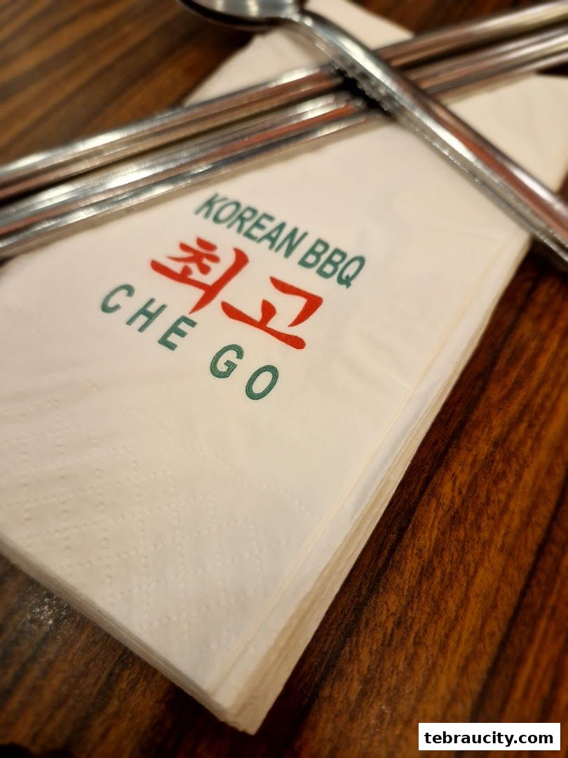 A stack of napkins with the Chego Korean BBQ logo and cutlery on a wooden table.