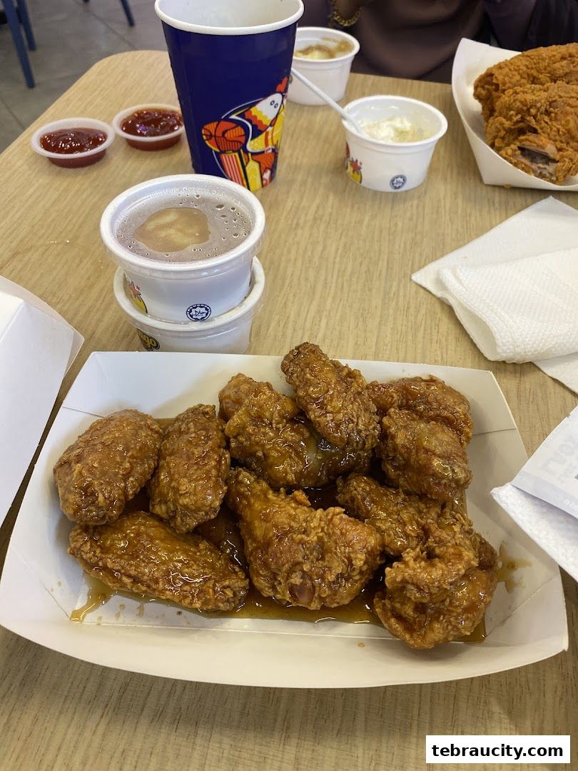 A tray of crispy, glazed chicken wings with dipping sauces and drinks on a table.