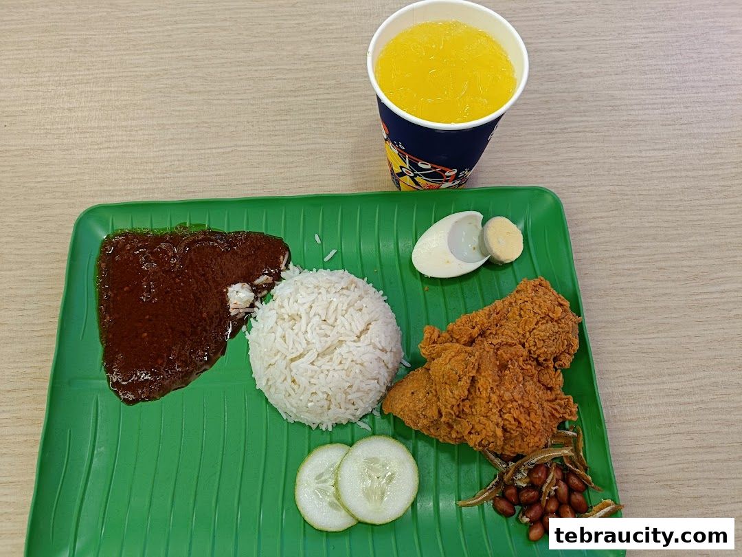 A plate of nasi lemak with fried chicken, sambal, rice, egg, peanuts, and anchovies, served with a drink.