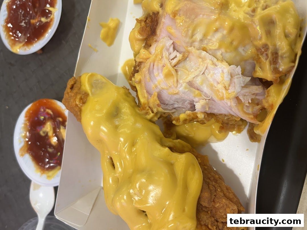Close-up of crispy fried chicken covered in melted cheese sauce with dipping sauces.