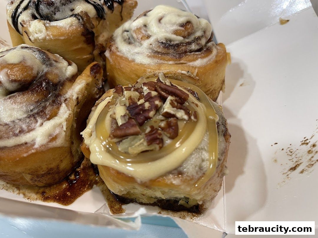 A close-up view of several freshly baked cinnamon rolls with various toppings in a white box.