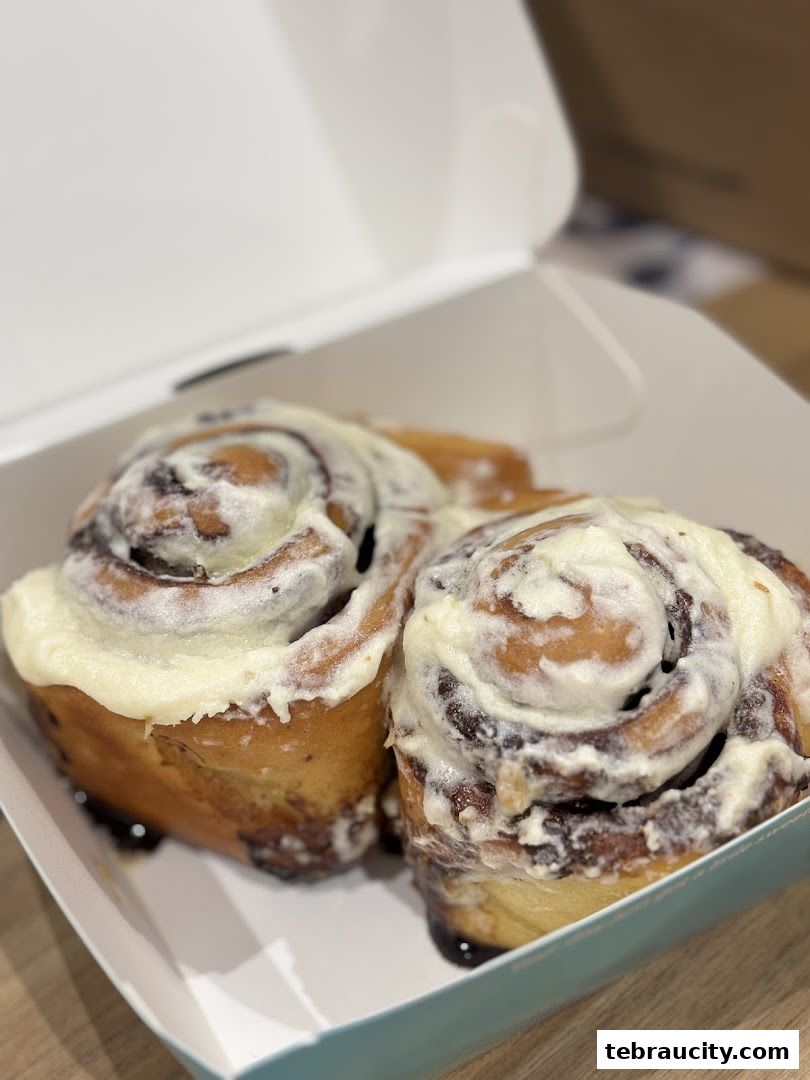 Two freshly baked Cinnabon cinnamon rolls with cream cheese frosting in a takeaway box.