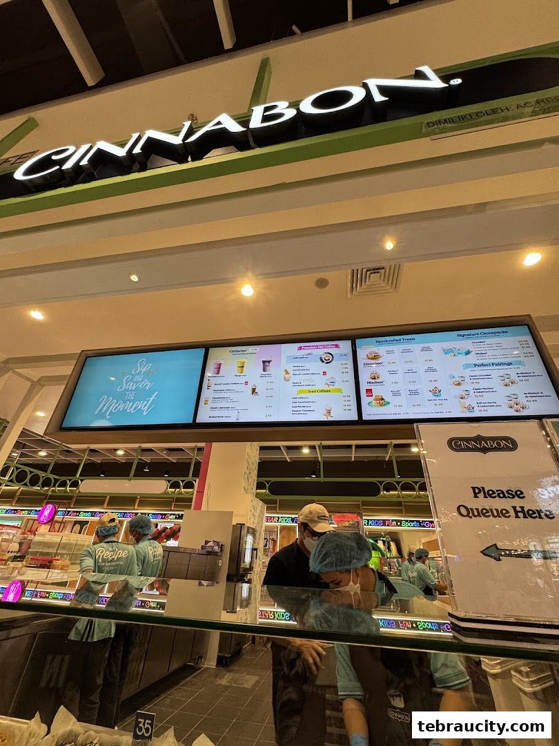 Interior view of a Cinnabon shop with staff and a digital menu board displaying various treats.