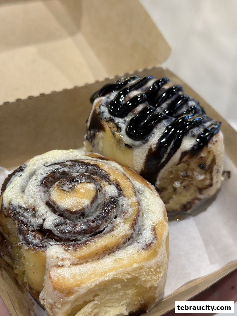 Two delicious Cinnabon cinnamon rolls, one with chocolate drizzle, in a take-out box.