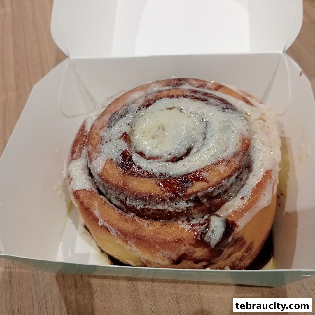A close-up of a freshly baked Cinnabon cinnamon roll in a white takeaway box.