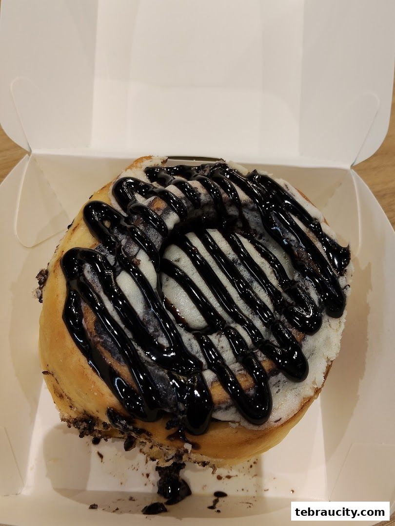 A close-up of a Cinnabon cinnamon roll with chocolate frosting in a white box.