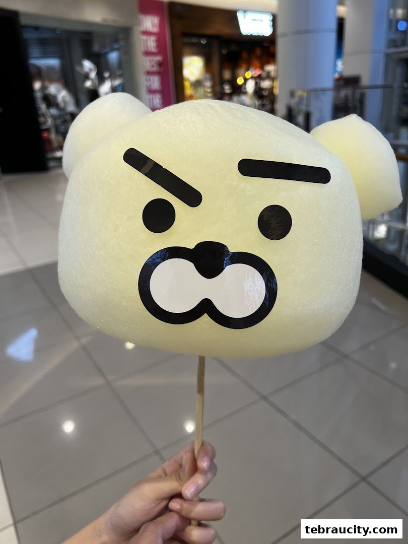 A hand holds a yellow cotton candy shaped like a cartoon bear face.