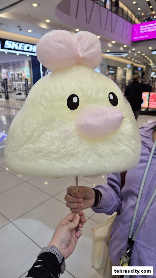 A person holds a large, yellow cotton candy shaped like a cute character.