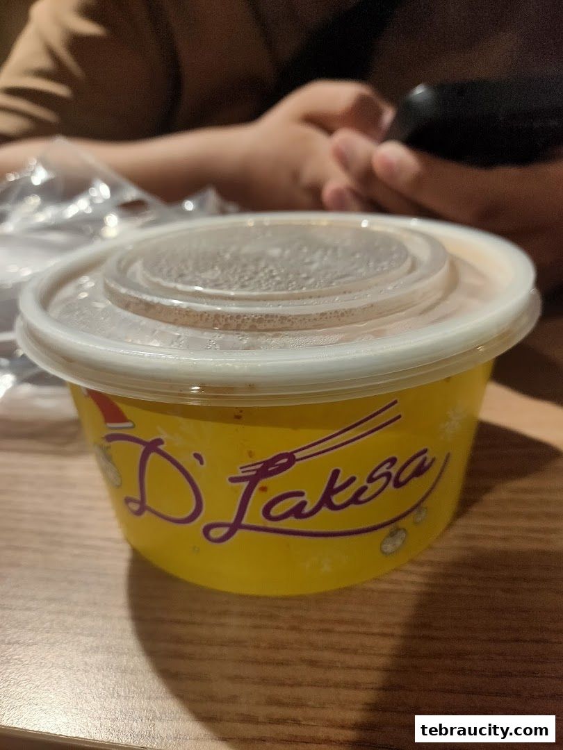 A close-up of a yellow takeout container with the D Laksa logo on it.