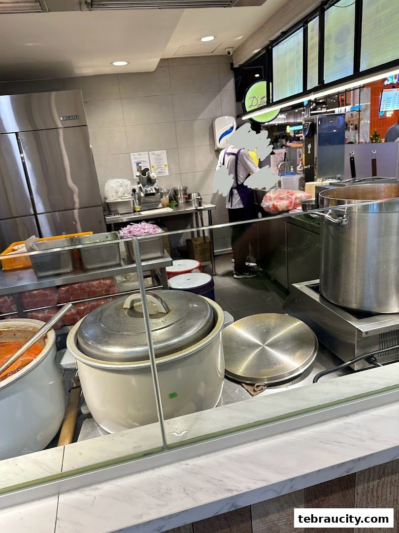 A busy kitchen scene at D Laksa, with staff preparing food and large cooking pots.