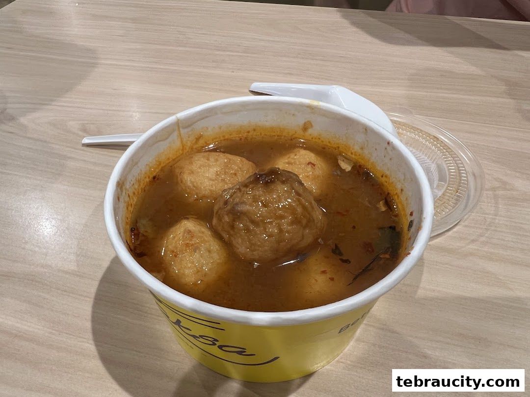 A bowl of Laksa with fish balls and a spoon on a wooden table.