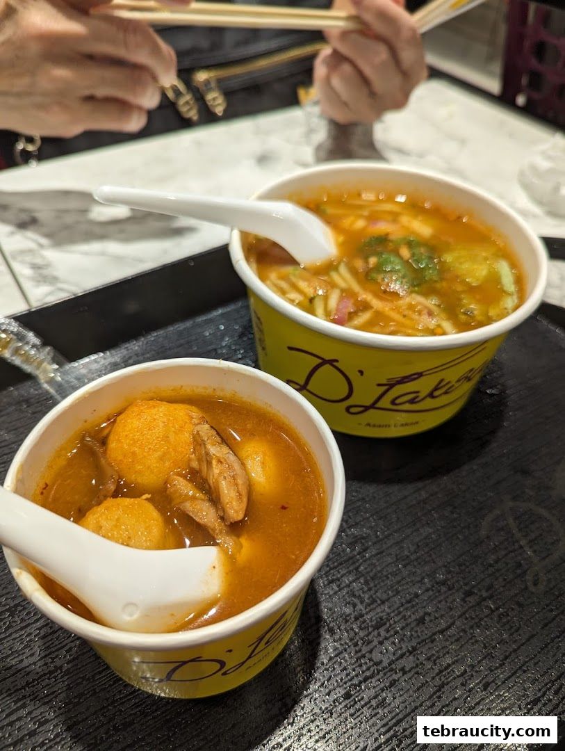 Two bowls of Laksa with spoons and chopsticks, served on a black tray.