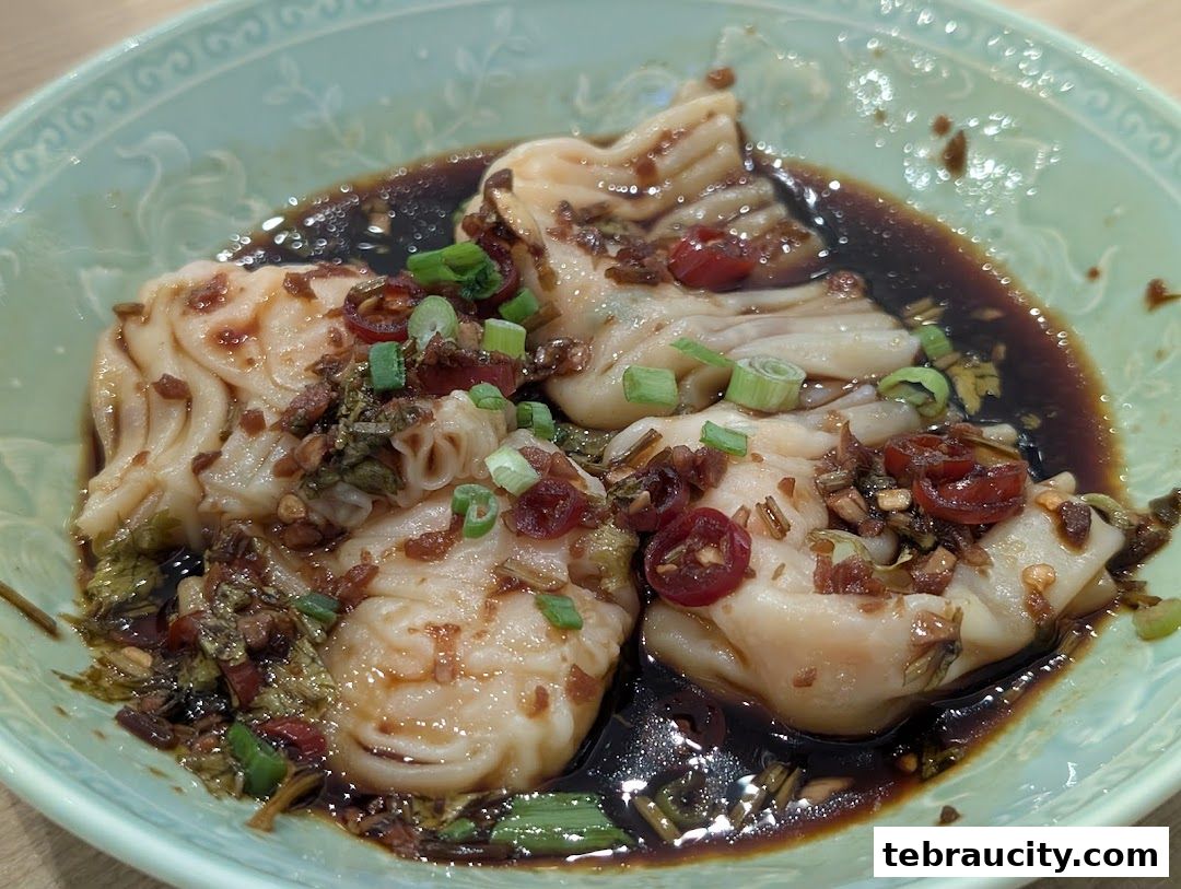 A close-up of dim sum dumplings in a savory sauce with chili and scallions.