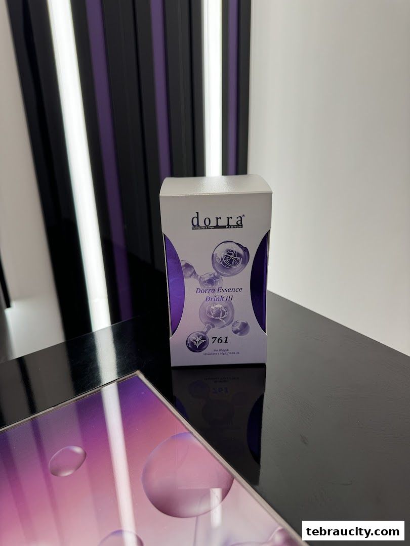 A box of Dorra Essence Drink III is displayed on a black surface with a purple and white background.