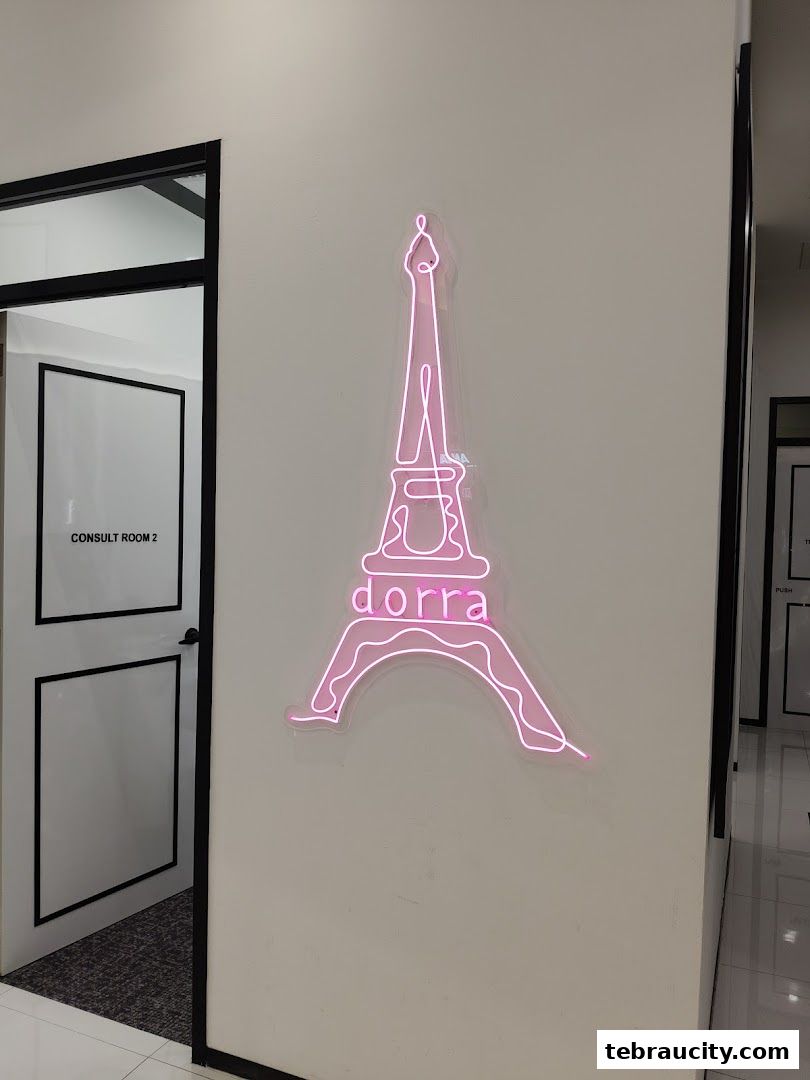 A pink neon Eiffel Tower sign with 'dorra' written on it hangs on a white wall.