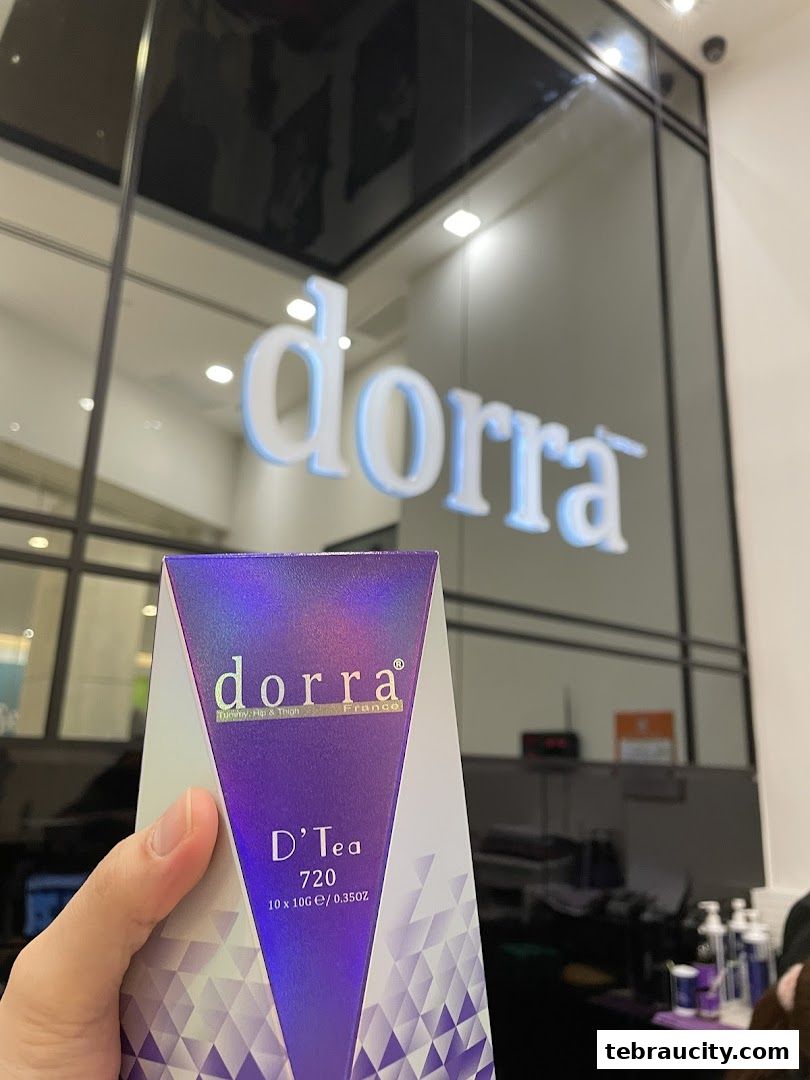 A hand holds a box of Dorra D'Tea in front of the shop's illuminated logo.