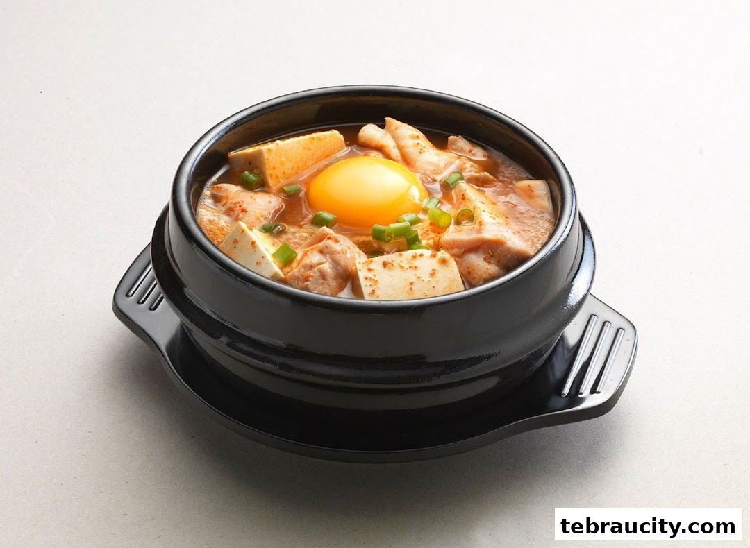A close-up shot of a steaming Korean Sundubu Jjigae with tofu, chicken, and a raw egg.