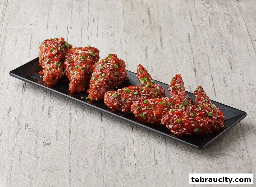 A platter of crispy Korean fried chicken wings coated in a sweet and spicy glaze, garnished with sesame seeds and chili flakes.