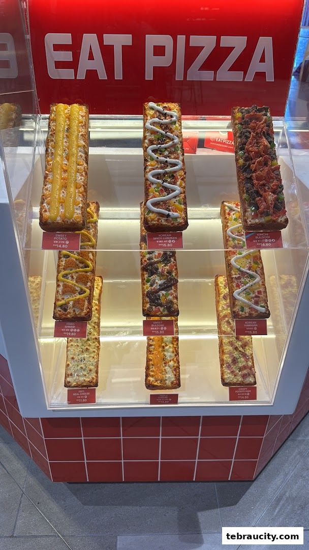 A display case filled with various rectangular pizzas with different toppings and prices.