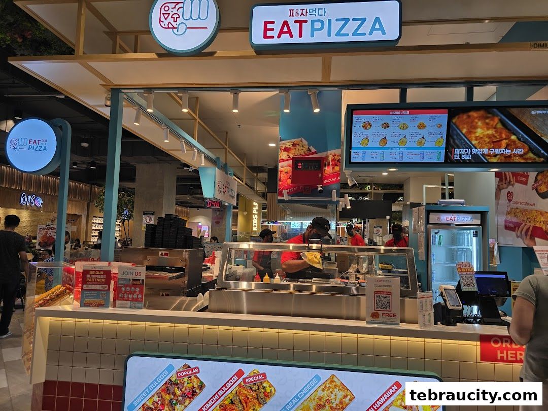 A vibrant pizza shop counter with staff preparing food and a digital menu displaying pizza options.