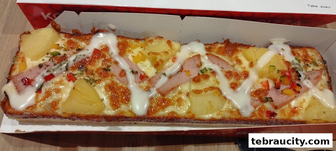 A long, rectangular pizza with ham, pineapple, and cheese in a white box.