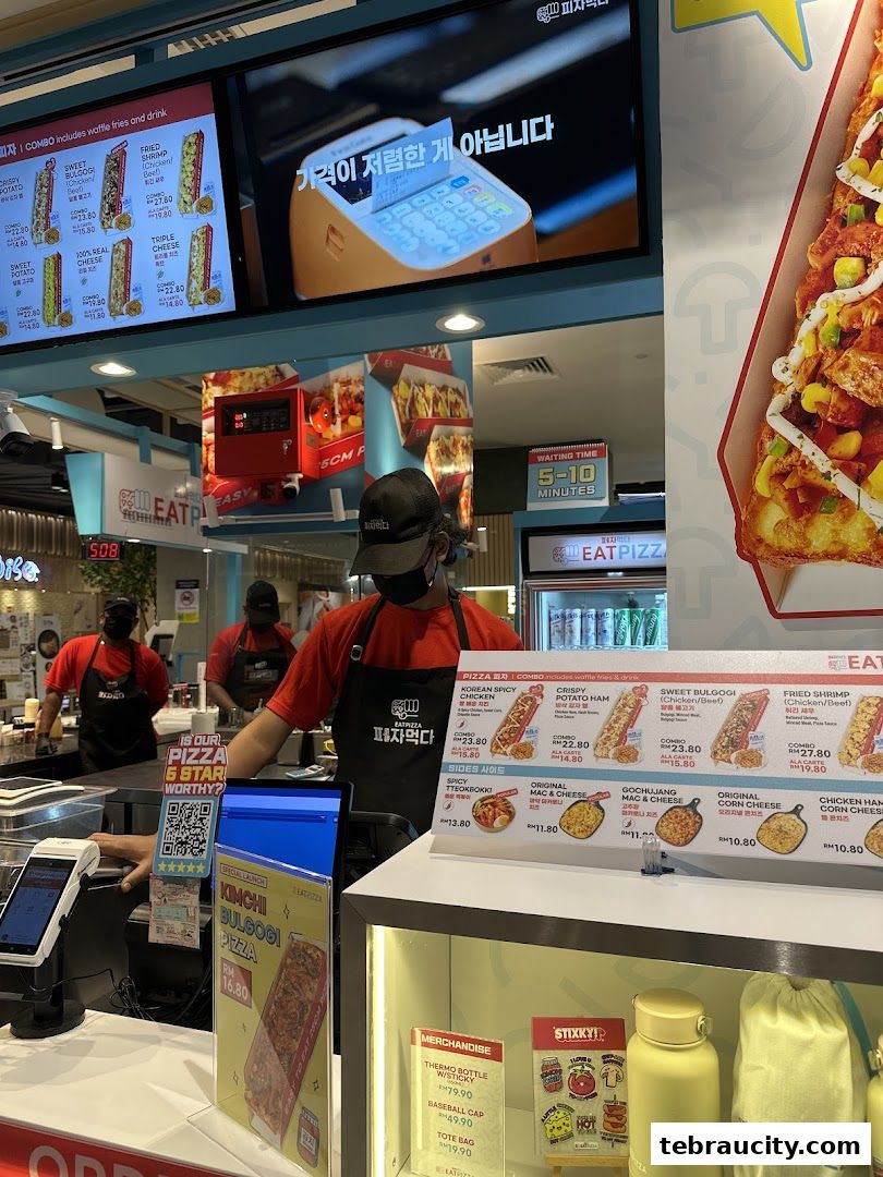 A pizza shop counter with staff, menu displays, and merchandise.