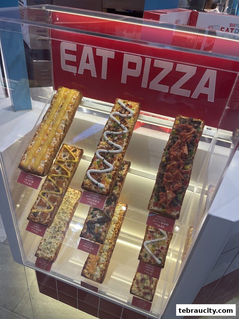 A display case filled with various rectangular pizzas with different toppings.