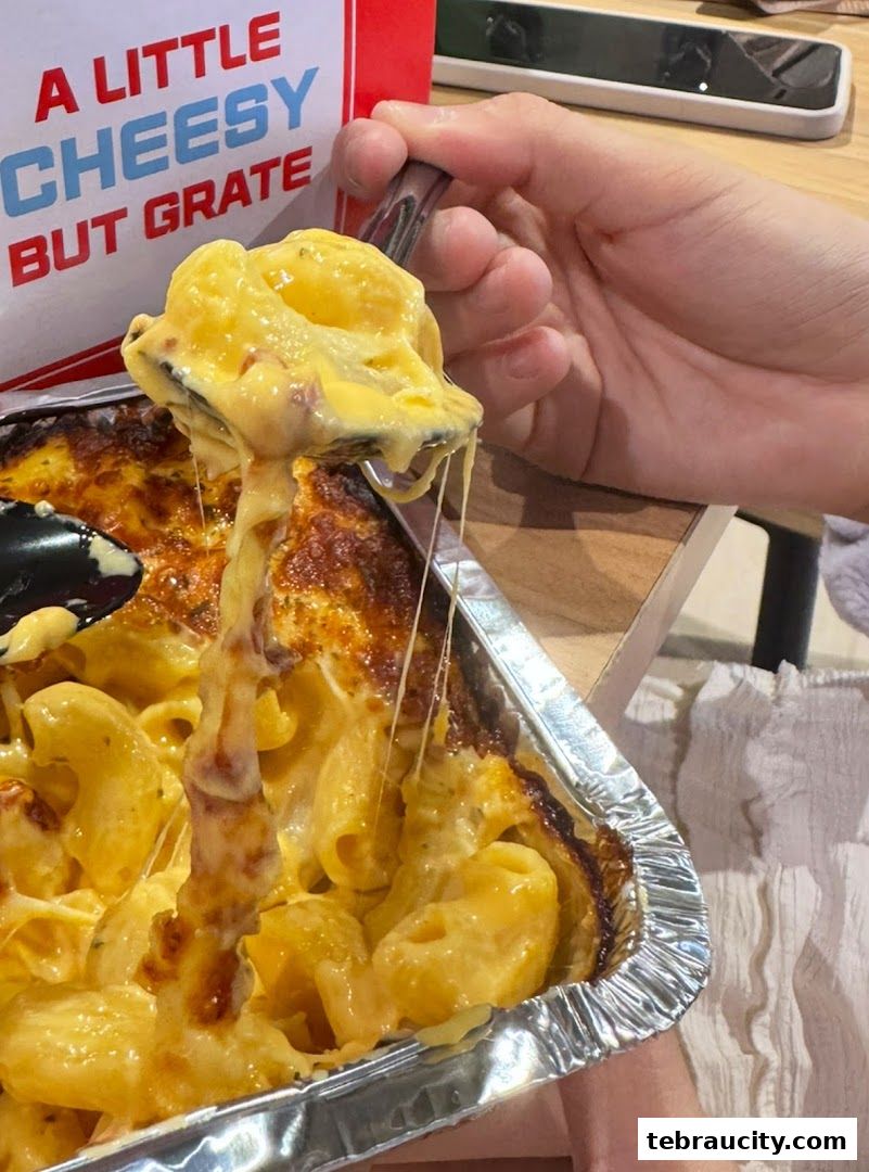 A close-up of cheesy macaroni being scooped from a foil container.