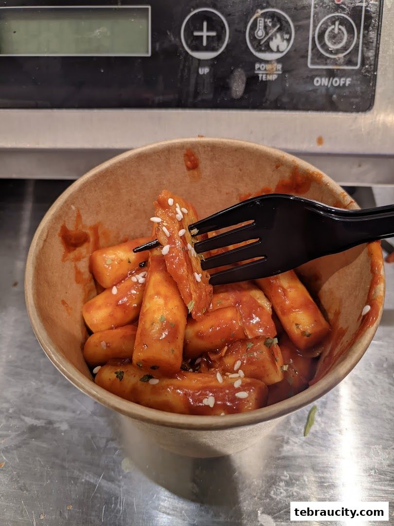 A bowl of Tteokbokki, Korean rice cakes in spicy sauce, topped with sesame seeds.