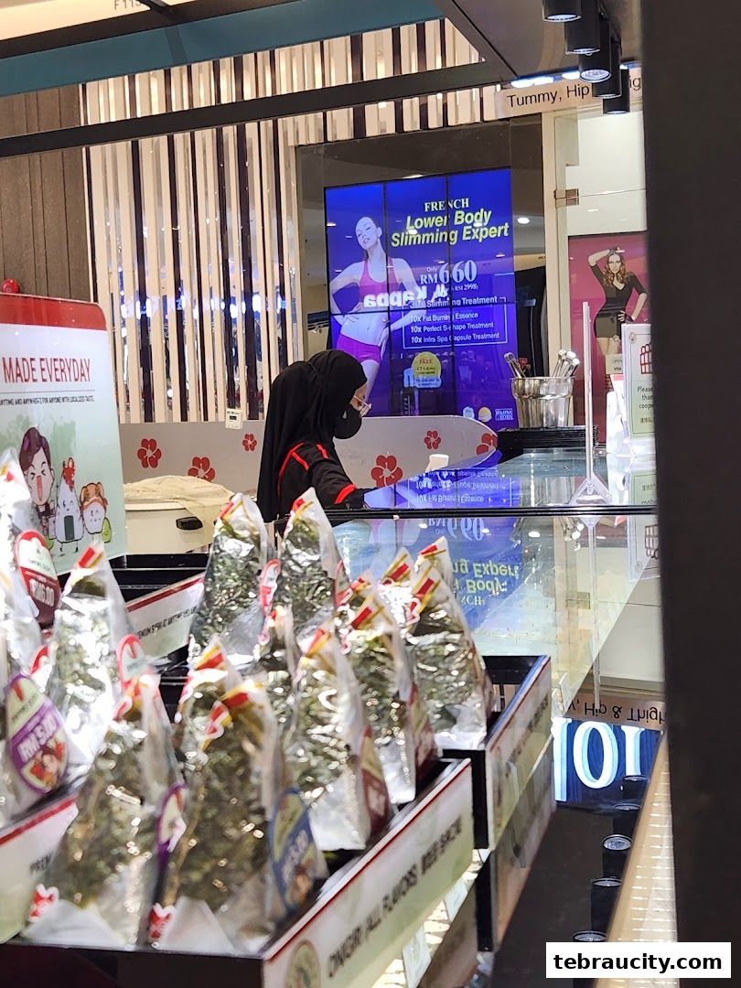 A display of packaged rice balls with a promotional screen in the background.