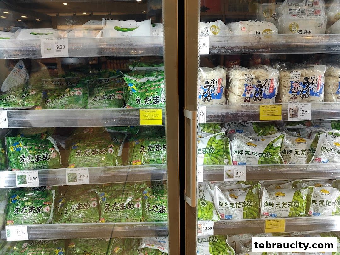 Frozen food products, including edamame and udon noodles, displayed in a supermarket refrigerator.