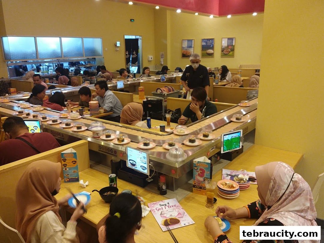 A busy sushi restaurant with customers seated at conveyor belt sushi tables.