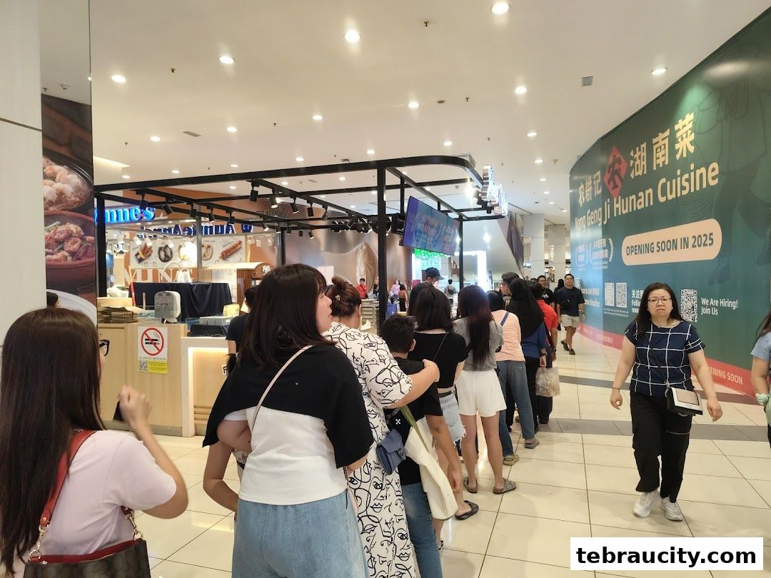A long queue of people waiting outside a shop with a large banner announcing a new opening.