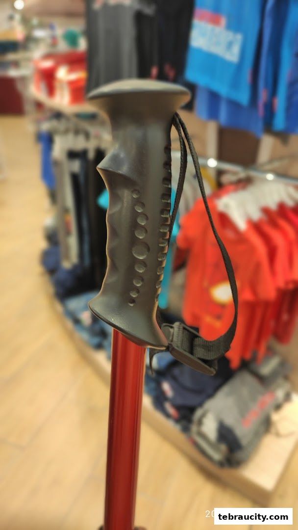 Close-up of a trekking pole handle with blurred clothing racks in the background.
