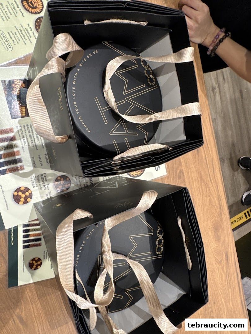 Two black gift bags from Fatmama Bakery containing round cookie tins with gold ribbon.