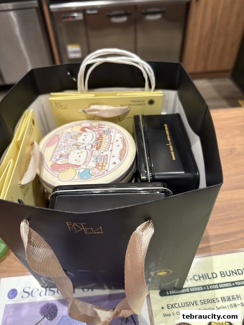 A black gift bag filled with various cookie tins and boxes from Fatmama Cookies.