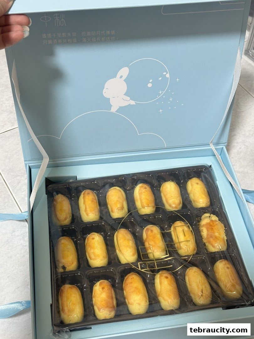 A light blue gift box filled with golden-brown pastries, decorated with a rabbit and moon motif.