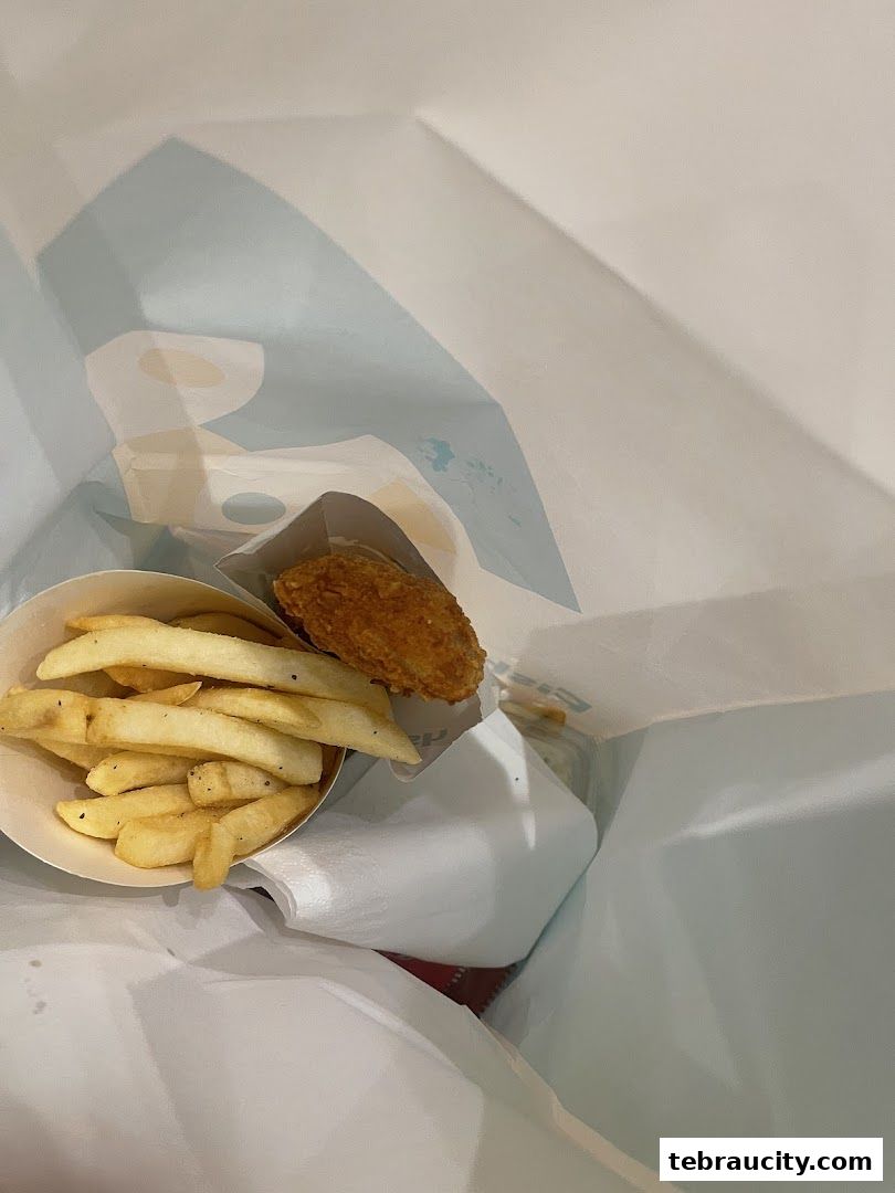 A paper bag contains french fries and a piece of fried chicken.