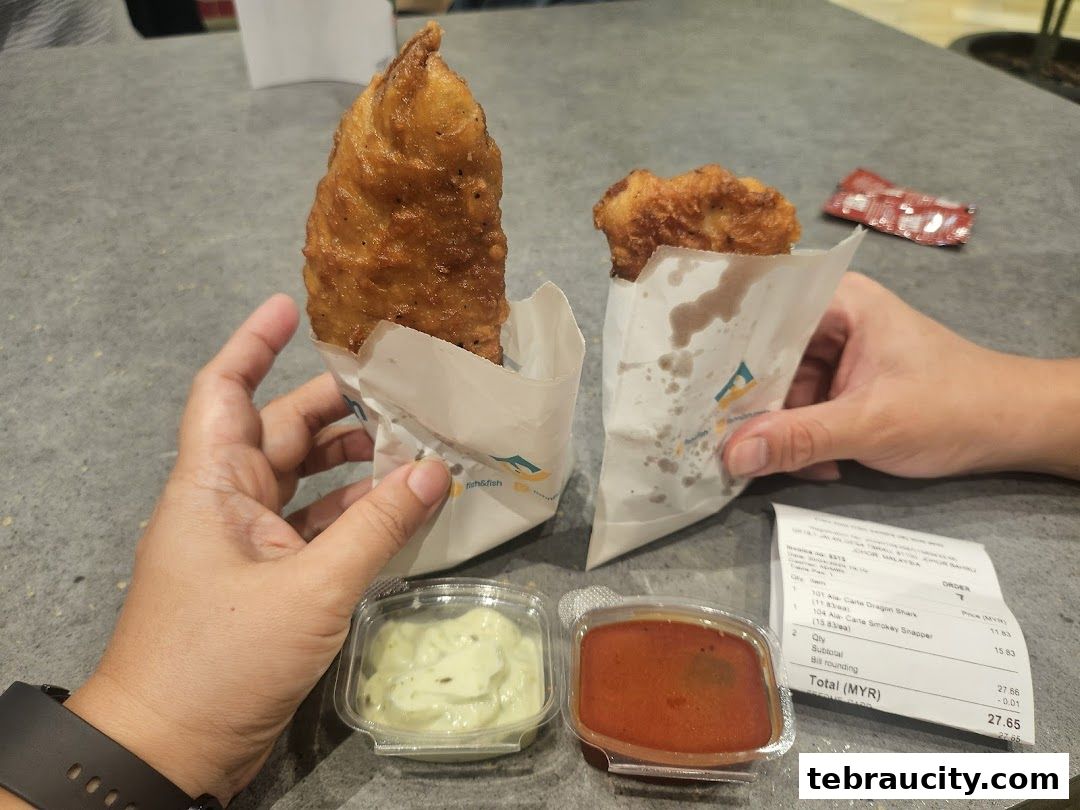 Two hands holding crispy fried fish pieces with dipping sauces and a receipt.