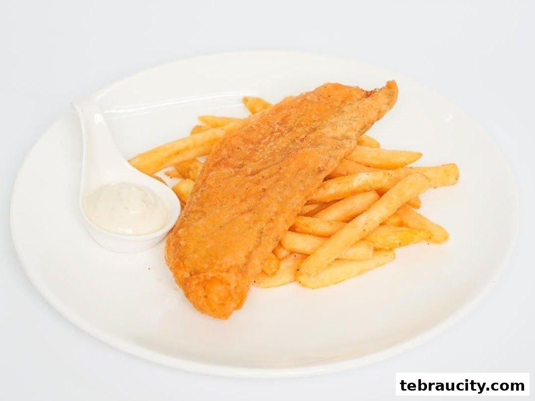 A plate of crispy fried fish and golden french fries with a side of dipping sauce.