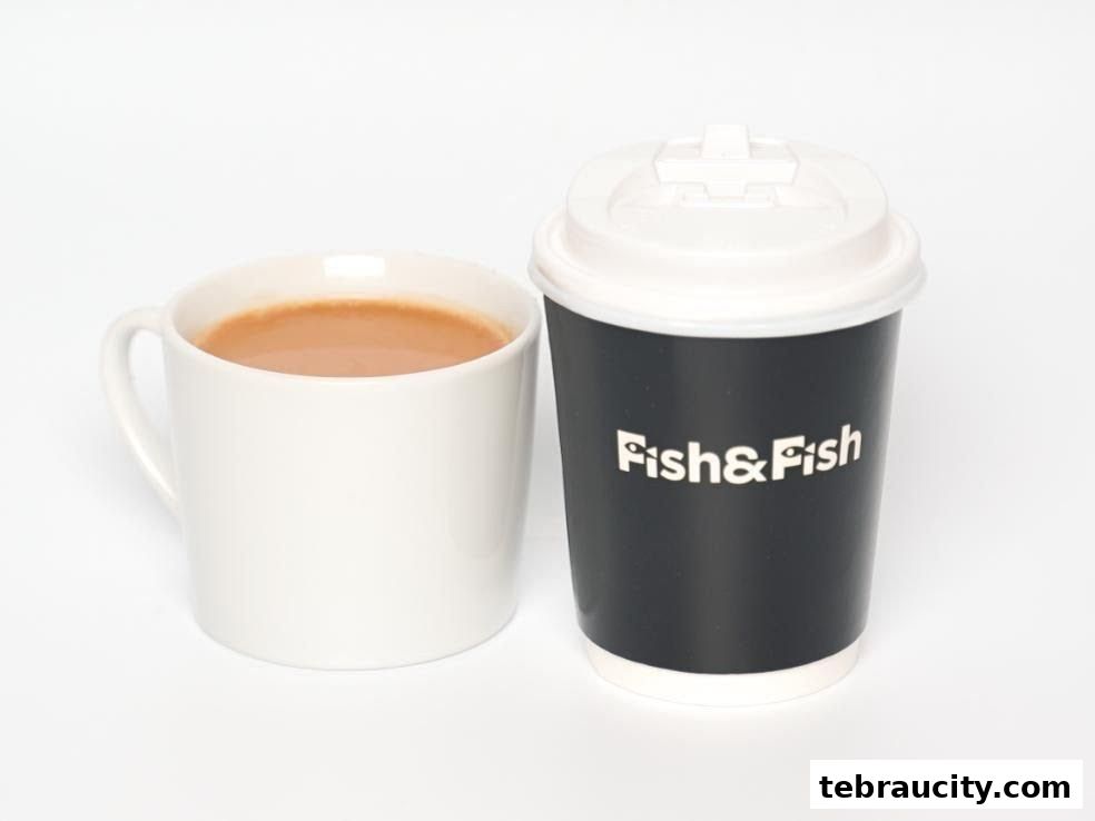 A white mug of tea sits next to a black to-go cup with the Fish & Fish logo.